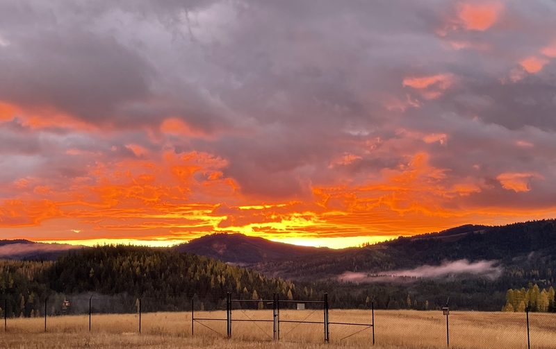 Fiery fall sunset over the ridgeline and valley fog above the fenced west meadow